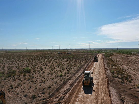 Large caterpillars driving on a dirt road with flat dirt landscape on the sides.