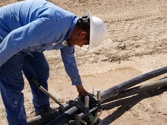 Man in white hard hat and blue shirt working on large rubber pipes.