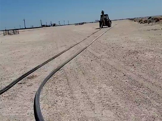 Large open white dirt field with a large long rubber hose.