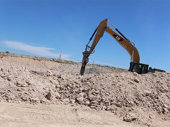 Heavy machine operate drilling equipment working in a white dirt field with lots of white gravel.