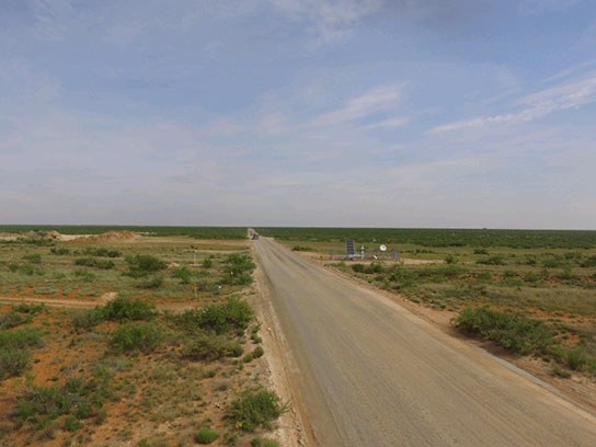 Long road leading into the distance with flat semi green land around it.