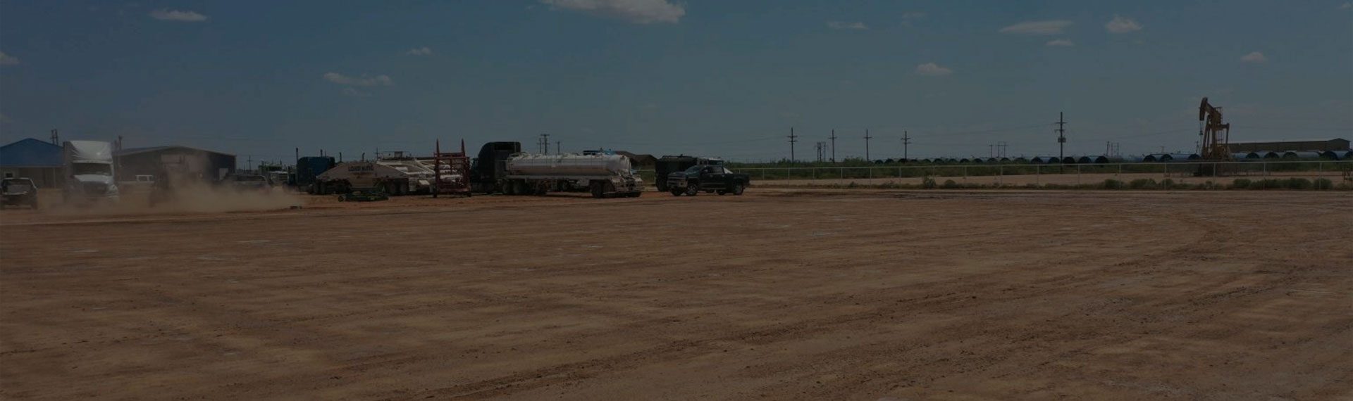 Large dirt field with lots of 18 wheelers in the distance.
