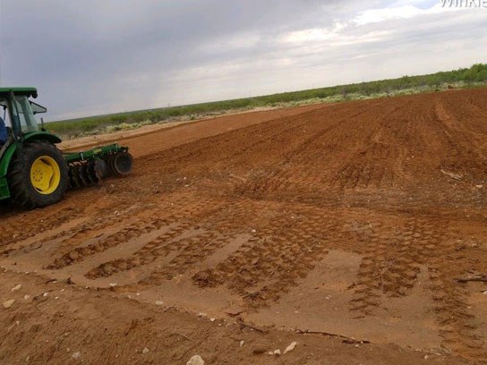 Large green tractor at work in a large open dirt field.