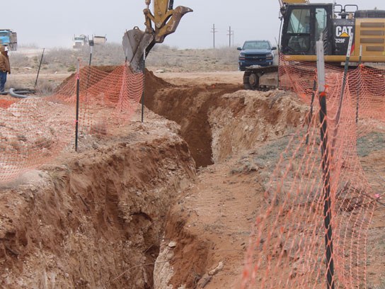 Large dirt pit with an orange safety fence surrounding it.