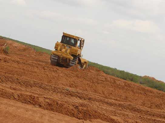 Large yellow heavy machinery with treads in a large dirt field.