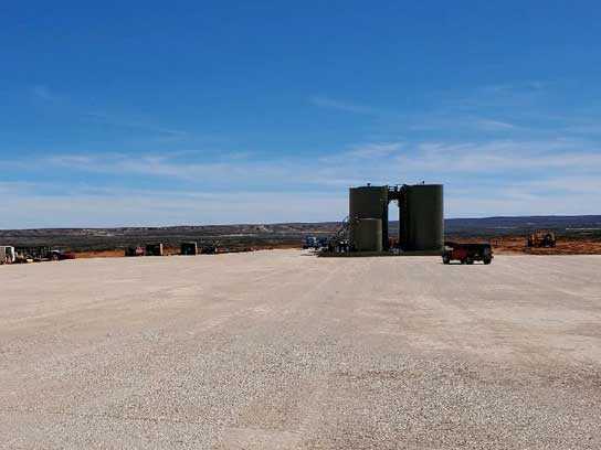Oilfield site with white dirt, two very large barrels, and a truck.