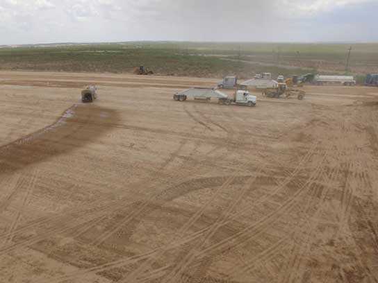 Large dirt field with lots of 18 wheelers and tire tracks.